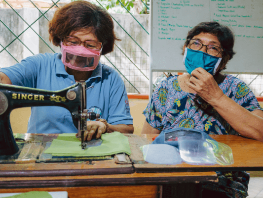 Two women in face masks sewing more face masks