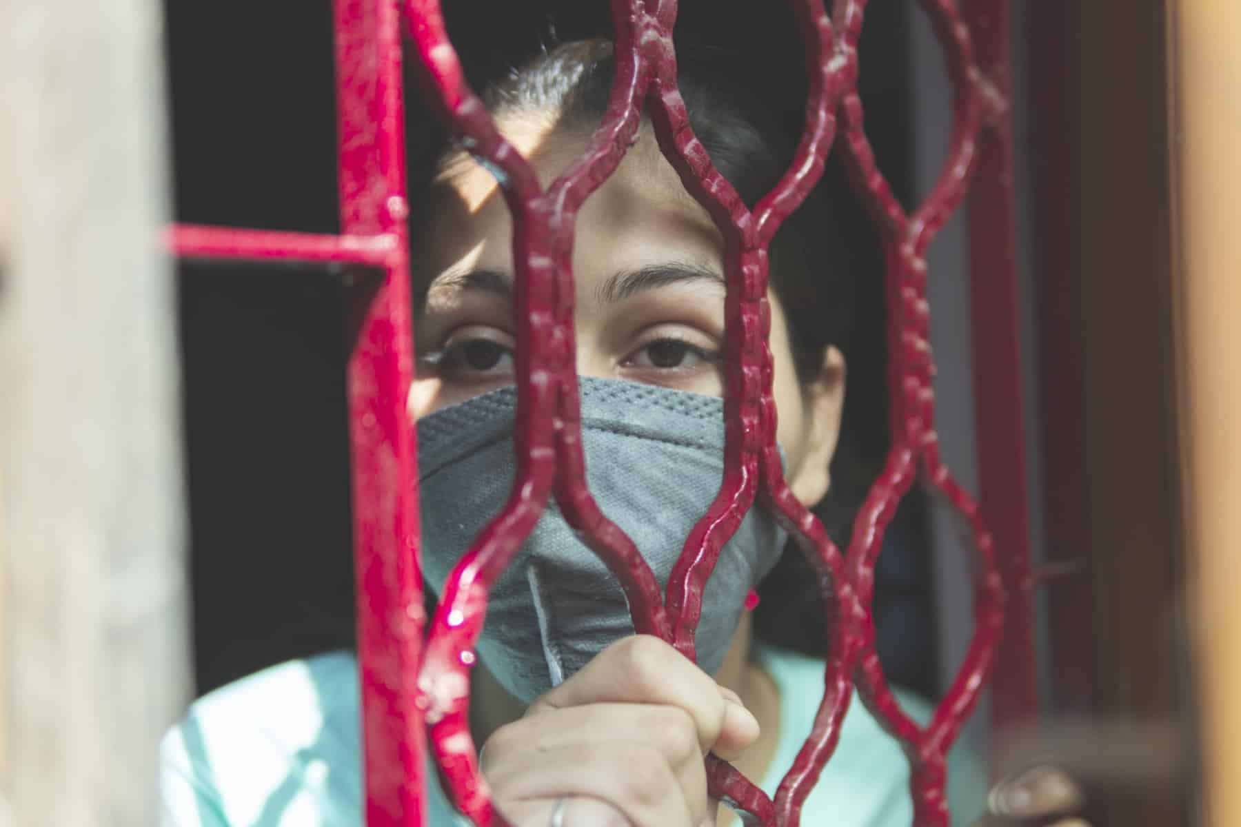 A woman in a mask looking through a fence wall
