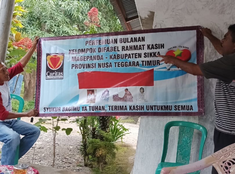 Two people hold up a sign advertising monthly meetings for a group for persons with disability